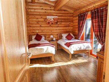 A bedroom with two single beds a nightstand and a door with red curtains at Rowan Lodge in Greetham Rutland