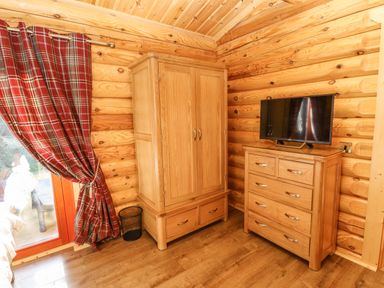 A wooden wardrobe and chest of drawers with a TV on top in a log cabin bedroom at Rowan Lodge in Greetham Rutland