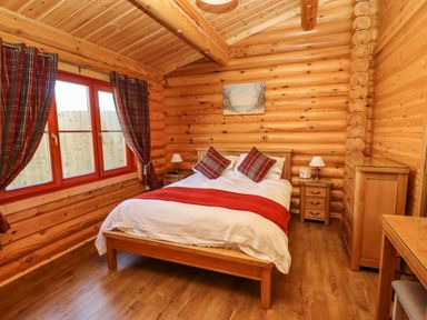 A bedroom with a bed two bedside tables lamps a chest of drawers and plaid curtains at Rowan Lodge in Greetham Rutland