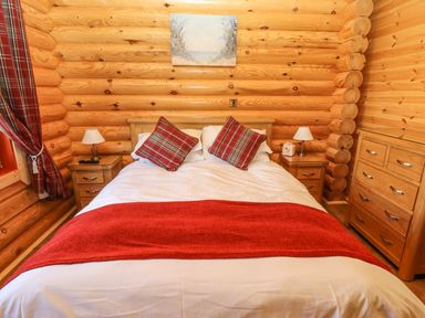 A bedroom with a double bed with red and plaid pillows and blankets and wooden furniture at Rowan Lodge in Greetham Rutland