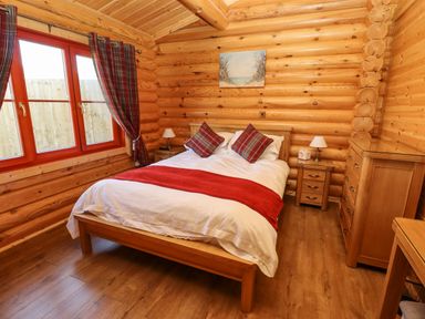 A bedroom with a wooden bed white bedding red accents and wooden furniture at Rowan Lodge Greetham Rutland