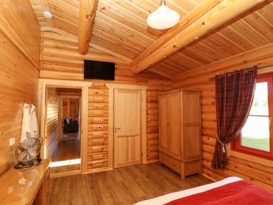 A wooden bedroom with a wardrobe fan and window with red curtains at Rowan Lodge in Greetham Rutland