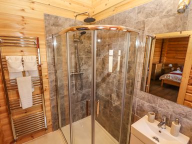 A bathroom with a corner glass shower enclosure a towel rack with towels and a sink with a mirror at Rowan Lodge in Greetham Rutland
