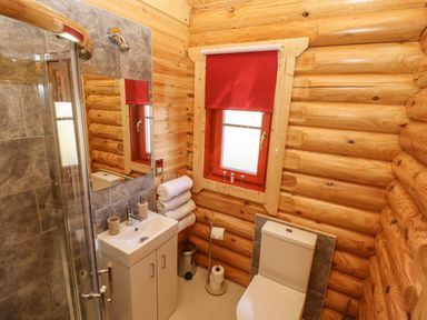 A bathroom with a toilet sink towels window with red blind and wooden log walls at Rowan Lodge in Greetham Rutland