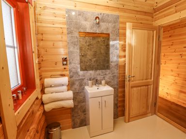 A bathroom with wooden walls white sink towels on a rack and a wooden door at Rowan Lodge in Greetham Rutland