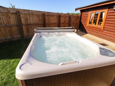 An outdoor hot tub with bubbling water next to a wooden fence and a wooden building with windows at Rowan Lodge in Greetham Rutland