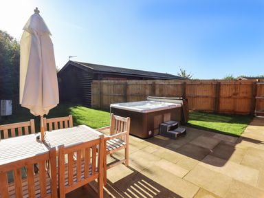 A backyard patio with a wooden dining table and chairs an umbrella a hot tub and a wooden fence at Rowan Lodge in Greetham Rutland