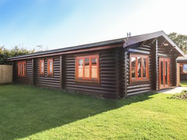 A wooden log cabin with several windows and a double door on a grassy lawn at Rowan Lodge in Greetham Rutland