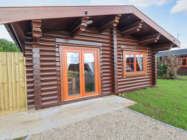A wooden log cabin with glass double doors and a window on a grassy area at Maple Lodge in Greetham Rutland