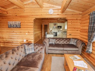 A living room with two brown sofas and a wooden coffee table opening to a kitchen at Maple Lodge in Greetham Rutland