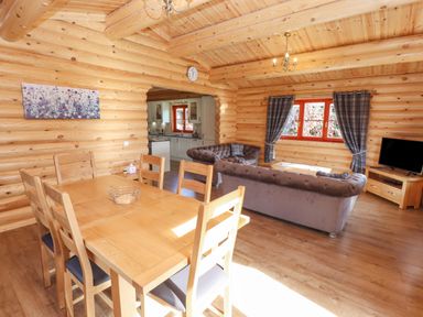 A wooden dining table with six chairs next to a living area with sofas television and window at Maple Lodge in Greetham Rutland