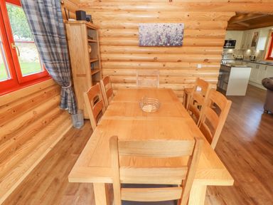 A dining area with a wooden table and six chairs beside a window with plaid curtains at Maple Lodge in Greetham Rutland