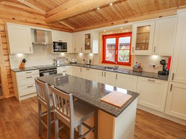 A kitchen with white cabinets a grey countertop two chairs and a wooden ceiling at Maple Lodge Greetham Rutland