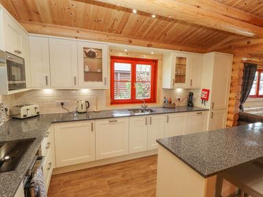 A kitchen with white cabinets grey countertops and a red window frame at Maple Lodge in Greetham Rutland