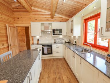 A kitchen with white cabinets black countertops wooden floor and a red window frame at Maple Lodge in Greetham Rutland