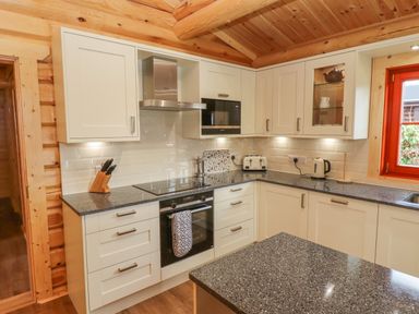 A kitchen with cream cabinets black countertop a stove oven microwave and a window at Maple Lodge in Greetham Rutland
