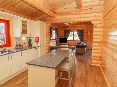 A kitchen with white cabinets and a gray countertop island with chairs opening to a living room with sofas and a television at Maple Lodge in Greetham Rutland