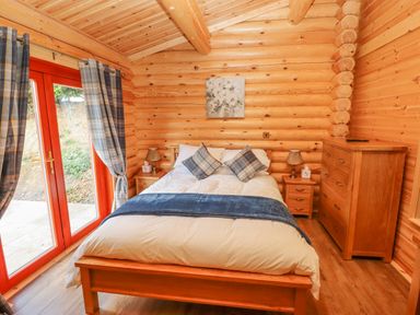 A bedroom with a double bed wooden furniture and plaid curtains at Maple Lodge in Greetham Rutland