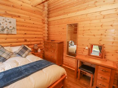 A bedroom with a bed blue blanket wooden dresser and vanity at Maple Lodge in Greetham Rutland