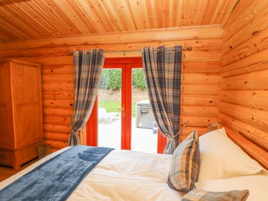 A bedroom with a wooden wardrobe bed and double doors with curtains at Maple Lodge in Greetham Rutland