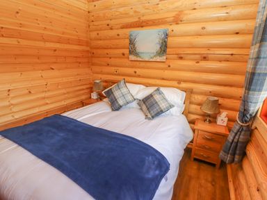 A bedroom with wooden walls a double bed blue blanket and two bedside tables at Maple Lodge in Greetham Rutland
