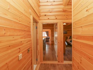 A wooden hallway with doors leading to a living room with a sofa and a bedroom with a bed at Maple Lodge in Greetham Rutland