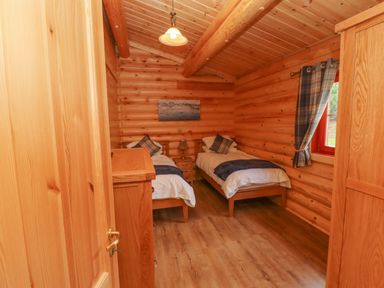 A bedroom with two single beds a nightstand a lamp a wooden dresser and a window with curtains at Maple Lodge in Greetham Rutland