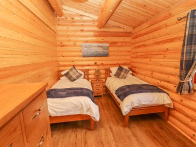 A bedroom with two single beds a nightstand a lamp a chest of drawers and a window with curtains at Maple Lodge in Greetham Rutland
