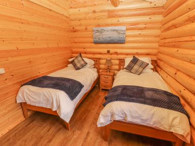 A bedroom with two single beds a small nightstand with a lamp and a painting on the wooden wall at Maple Lodge in Greetham Rutland
