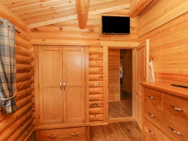 A wooden room with a wardrobe, dresser, mounted TV, and a doorway at Maple Lodge Greetham Rutland