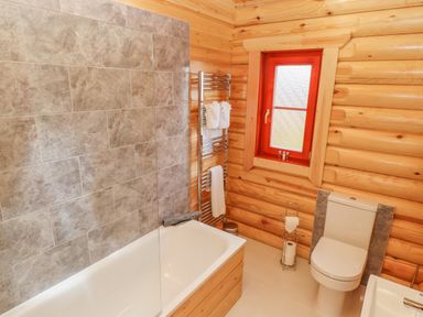 A bathroom with wooden walls a bathtub a toilet a window and a towel rack at Maple Lodge in Greetham Rutland
