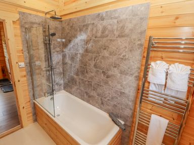 A bathroom with a bathtub shower combination and tiled wall with wooden paneling and a towel rack at Maple Lodge in Greetham Rutland