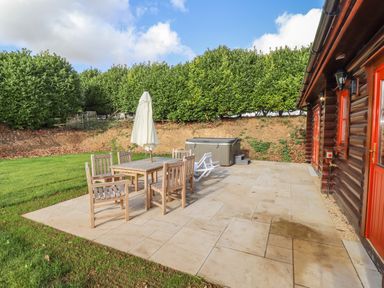An outdoor patio with wooden table and chairs an umbrella and a hot tub next to a wooden building at Maple Lodge in Greetham Rutland