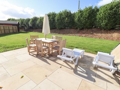 An outdoor patio with wooden table and chairs white loungers and green lawn at Maple Lodge in Greetham Rutland