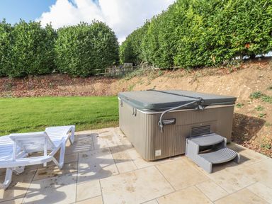 An outdoor area with a hot tub and two white lounge chairs on a tiled patio at Maple Lodge in Greetham Rutland