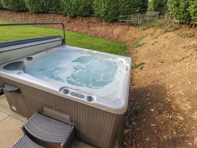 An outdoor hot tub with bubbling water on a tiled surface next to a grass lawn and a dirt slope at Maple Lodge in Greetham Rutland