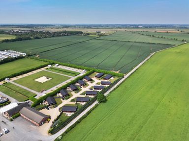 An aerial view of a rural property with multiple small buildings surrounded by green fields at Maple Lodge in Greetham Rutland