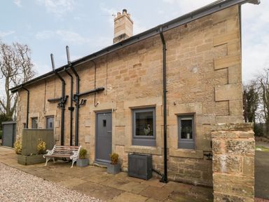 Stone exterior of a cottage with gray doors and windows and a bench at Grange Cottages in Alnwick