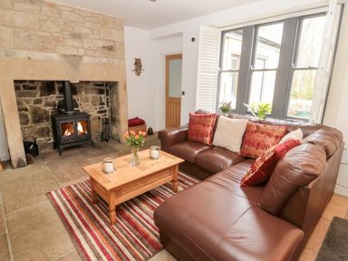 A living room with a leather sofa and a wooden coffee table in front of a stone fireplace at Grange Cottages in Alnwick