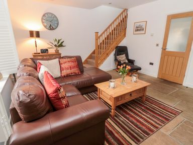 A living room with a brown leather sofa a wooden coffee table with flowers on a striped rug and a staircase at Grange Cottages in Alnwick