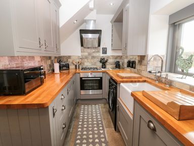 A kitchen with wooden countertops grey cabinets a stove microwave washing machine and a window at Grange Cottages in Alnwick