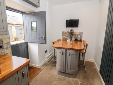 A kitchen dining area with a wooden table and chairs a half-open door and a wall-mounted television at Grange Cottages in Alnwick