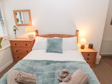 A bedroom with a double bed with white and teal bedding bedside tables with lamps and a mirror on the wall at Grange Cottages in Alnwick