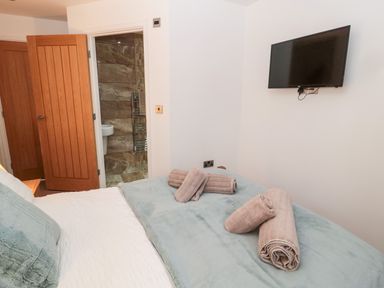 A bedroom with a bed with rolled towels on it a wall-mounted television a wooden door and a bathroom with tiled walls at Grange Cottages in Alnwick