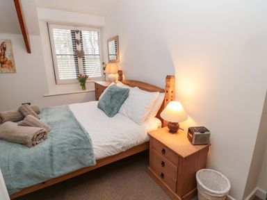 A bedroom with a wooden bed side tables lamps and a window with blinds at Grange Cottages in Alnwick
