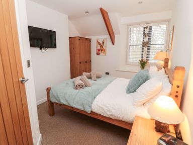 A bedroom with a wooden bed and bedside table a window and a wall-mounted television at Grange Cottages Alnwick