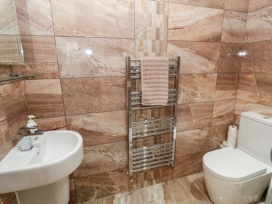 A bathroom with a sink soap dispenser towel rack with towel and a toilet at Grange Cottages in Alnwick