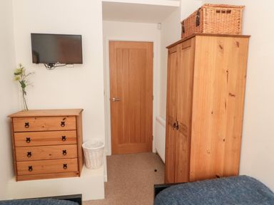 A bedroom with a wooden wardrobe and chest of drawers a wall-mounted television and a wooden door at Grange Cottages in Alnwick