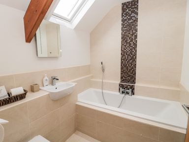 A bathroom with a bathtub with a handheld shower head a wall-mounted sink and a skylight window at Grange Cottages in Alnwick