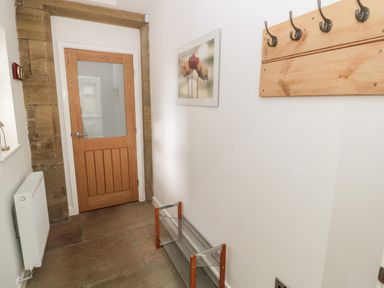 A hallway with a wooden door a shoe rack a coat rack a wall painting and a radiator at Grange Cottages in Alnwick